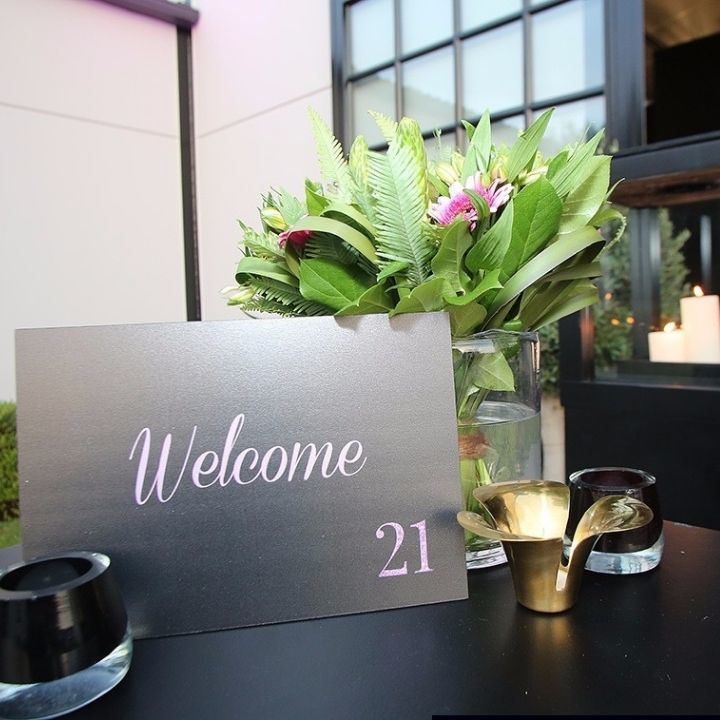 Affiche Welcome 21 posé sur une table noir et des fleurs vertes