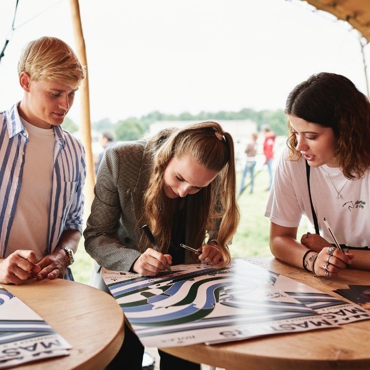 Trois personnes signent une affiche sur une table en bois